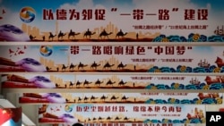 In this June 29, 2018, photo, a man stands underneath the pillars displaying Chinese President Xi Jinping's signature "China Dream" and "One Belt, One Road" foreign policy plan during an event in Beijing.