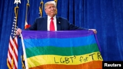 Donald Trump memegang bendera pelangi bertuliskan "LGBTs for TRUMP" saat masih berkampanye, di Greeley, Colorado, Oktober 2016.