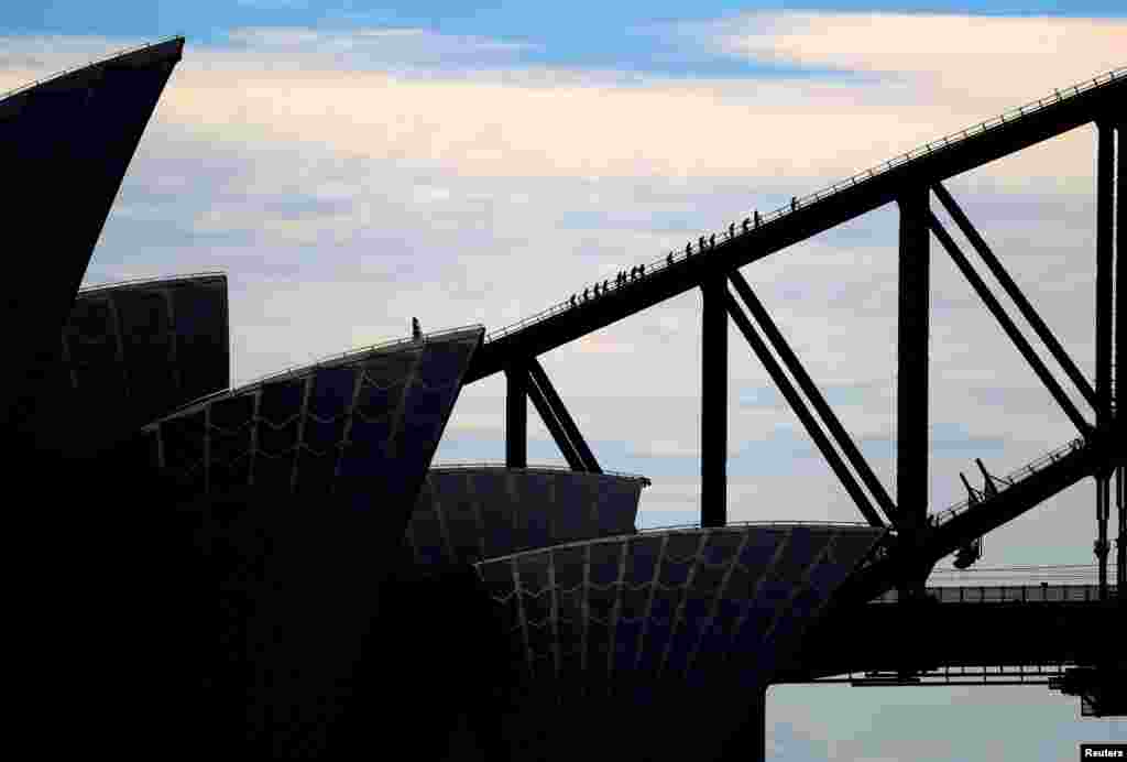 The roof of the Sydney Opera house can be seen in front of tourists as they climb the Sydney Harbour Bridge in Australia.