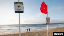 Dua orang pria berjalan di pinggir pantai Newcastle, Australia, melewati papan peringatan larangan beraktivitas di laut dan ancaman ikan hiu (Foto: dok). Seorang warga Jepang tewas, setelah seekor ikan hiu mencabik kedua kakinya, Senin (9/2), ketika berselancar di lepas pantai pantai timur Australia. 