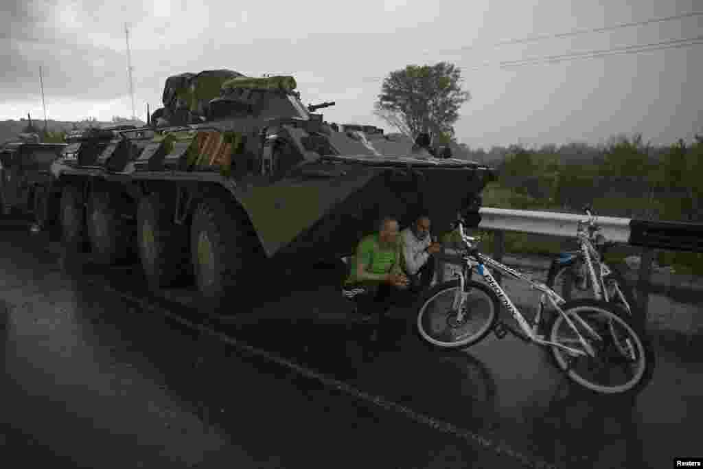 Civilians find cover from the rain under a Ukrainian army armored personnel carrier at a checkpoint near the town of Slaviansk.