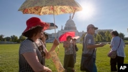 Visitors from Korea shield themselves from the early morning sun as they tour the Capitol in Washington, Aug. 12, 2016. 