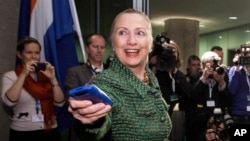 In this Dec. 8, 2011, file-pool photo, then-Secretary of State Hillary Clinton hands off her mobile phone after arriving for a meeting in The Hague, Netherlands. (AP Photo/J. Scott Applewhite, FILE)