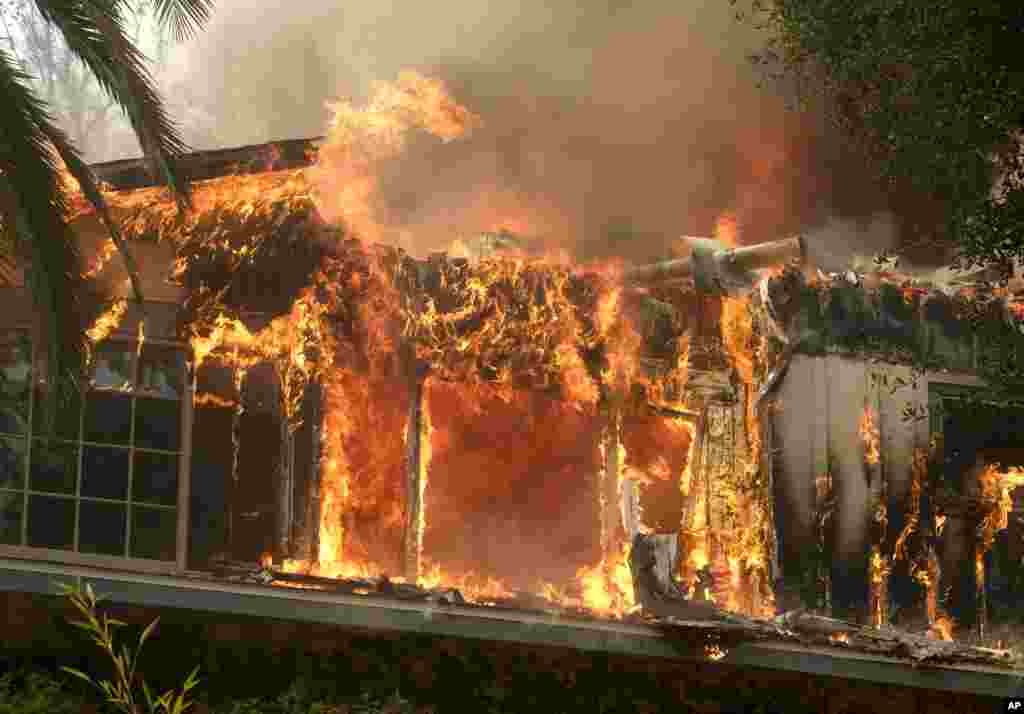 FILE - The Woolsey Fire burns a home near Malibu Lake in Malibu, Calif., Nov. 9, 2018. The fast-moving flames the total evacuation of the celebrity enclave.