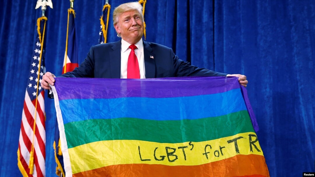 Donald Trump memegang bendera pelangi bertuliskan "LGBTs for TRUMP" saat masih berkampanye, di Greeley, Colorado, Oktober 2016.
