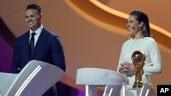 FILE - Former American soccer international Carli Lloyd, right, and Jermaine Jenas, English television presenter, pundit and retired professional soccer player assist with the 2022 soccer World Cup draw at the Doha Exhibition and Convention Center in Doha, Qatar, April 1, 2022.