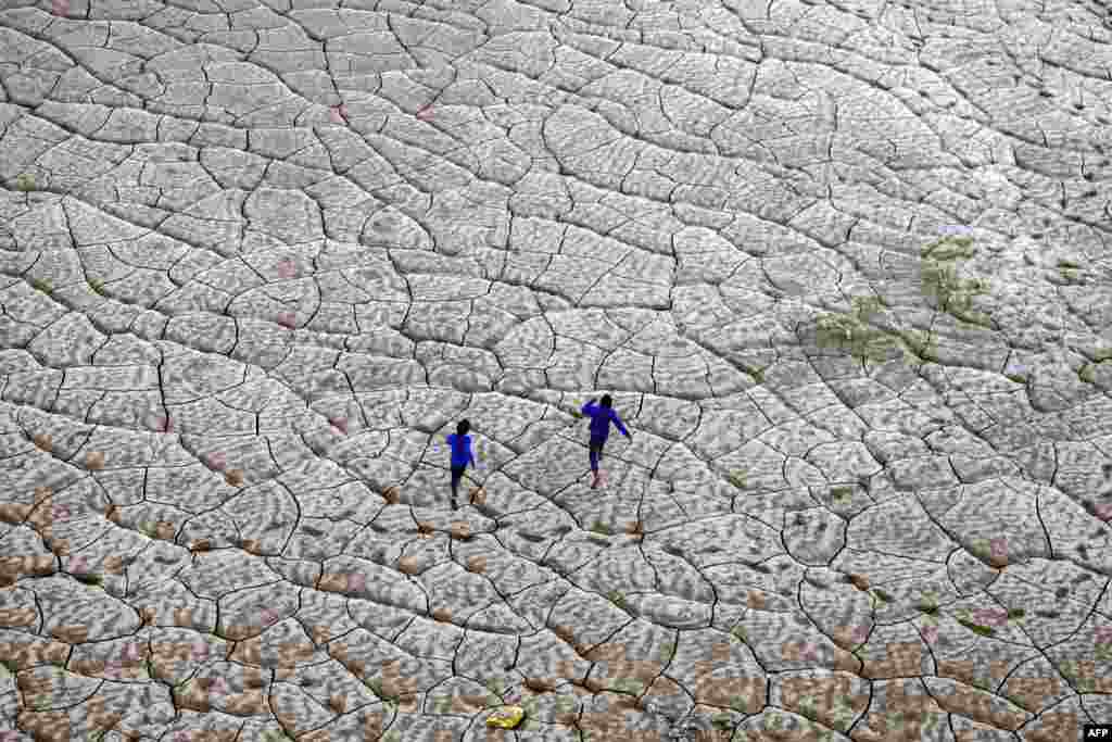 Boys run along the dried-up portion of a riverbed on the banks of river Ganges in Prayagraj, India.