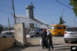 Palestinians walk past an Israeli military guard tower with two robotic guns and surveillance cameras at the Aroub refugee camp in the West Bank, Thursday, Oct. 6, 2022.(AP Photo/Mahmoud Illean)