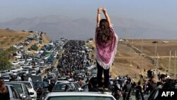 FILE - This UGC image posted on Twitter reportedly on Oct. 26, 2022 shows an unveiled woman standing atop a vehicle as thousands make their way towards a cemetery in Mahsa Amini's hometown to mark 40 days since her death.