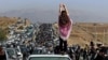 FILE - This UGC image posted on Twitter reportedly on Oct. 26, 2022 shows an unveiled woman standing atop a vehicle as thousands make their way towards a cemetery Mahsa Amini's hometown to mark 40 days since her death.
