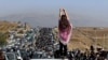 FILE - This UGC image posted on Twitter reportedly on Oct. 26, 2022, shows an unveiled woman overlooking thousands making their way toward a cemetery in Mahsa Amini's hometown. An increasing number of women in Iran are defying Iran's compulsory dress code by not wearing hijabs. 