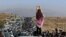 FILE - This UGC image posted on Twitter reportedly on Oct. 26, 2022, shows an unveiled woman overlooking thousands making their way toward a cemetery in Mahsa Amini's hometown. An increasing number of women in Iran are defying Iran's compulsory dress code by not wearing hijabs. 