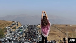 FILE - This UGC image posted on Twitter reportedly on Oct. 26, 2022 shows an unveiled woman standing atop a vehicle as thousands make their way towards a cemetery Mahsa Amini's hometown to mark 40 days since her death.