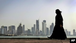 FILE- A Qatari woman walks in front of the city skyline in Doha, Qatar, May 14, 2010. After FIFA awarded the World Cup to Qatar, there were questions about what women would be allowed to wear. A local guide says women must dress modestly with sleeves, long pants or long skirts.