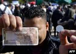 A man shows a Syrian pound in the form of a coin as well as a banknote, at a shopping festival in the Syrian capital Damascus on Jan. 22, 2020.