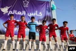Anak-anak yang mengenakan seragam tim sepak bola nasional Qatar berpose saat pembukaan "Camps World Cup" di Stadion Kota Idlib yang baru dibuka kembali pada 19 November 2022. (Foto : AFP)