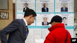 A member of the election commission, left, speaks to a voter in front of an election poster with photos and biographies of presidential candidates at a polling station in Almaty, Kazakhstan, Nov. 20, 2022. President Kassym-Jomart Tokayev is pictured in the bottom row, center.