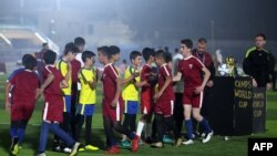 Anak-anak yang mengenakan kaus tim sepak bola nasional Qatar dan Ekuador berjabat tangan sebelum pertandingan pembukaan "Camps World Cup" di Stadion Kota Idlib yang baru dibuka kembali di kota Suriah barat laut pada 19 November 2022. (Foto : AFP)