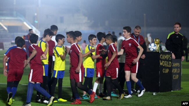 أطفال يرتدون قمصان منتخبي قطر والإكوادور لكرة القدم يتصافحون قبل المباراة الافتتاحية لـ "كأس العالم للمعسكرات" في ملعب إدلب البلدي الذي أعيد افتتاحه حديثًا في المدينة الواقعة شمال غرب سوريا التي يسيطر عليها المتمردون في 19 تشرين الثاني / نوفمبر 2022.