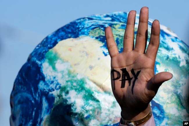 A hand of a protester reads "pay" amid calls for reparations for loss and damage at the COP27 U.N. Climate Summit, in Sharm el-Sheikh, Egypt, Nov. 18, 2022. (AP Photo/Peter Dejong)