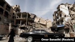 A woman walks past a vehicle parked near damaged buildings in Douma, in the eastern suburbs of Damascus, March 9, 2021. (Omar Sanadiki /Reuters) 