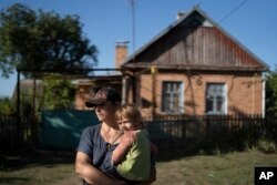 FILE - Natalia Stokoz holds her daughter Veronika, 3, as they stand near their house in the village of Zorya, about 20 kilometers from the Zaporizhzhia nuclear power plant, Sept. 2, 2022. (AP Photo/Leo Correa)