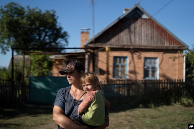 FILE - Natalia Stokoz holds her daughter Veronika, 3, as they stand near their house in the village of Zorya, about 20 kilometers from the Zaporizhzhia nuclear power plant, Sept. 2, 2022. (AP Photo/Leo Correa)