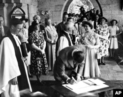 FILE - Britain's Princess Elizabeth talks with the Bishop of Mombasa while her husband, Prince Philip, the Duke of Edinburgh signs the visitors book at All Saints Cathedral, in Nairobi, on Feb. 2, 1952.