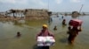 Women carry belongings from their flooded home after monsoon rains, in the Qambar Shahdadkot district of Sindh province, Pakistan, Sept. 6, 2022. Millions have lost their homes in flooding this year that many experts have blamed on climate change.