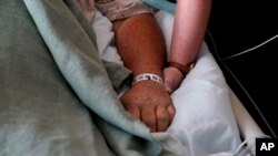 FILE - A woman, who is on oxygen as she recovers from COVID-19, holds the hand of her husband, who also contracted COVID-19, as he is kept alive with the help of an oxygenation machine at a medical center in Shreveport, La., Aug. 18, 2021.