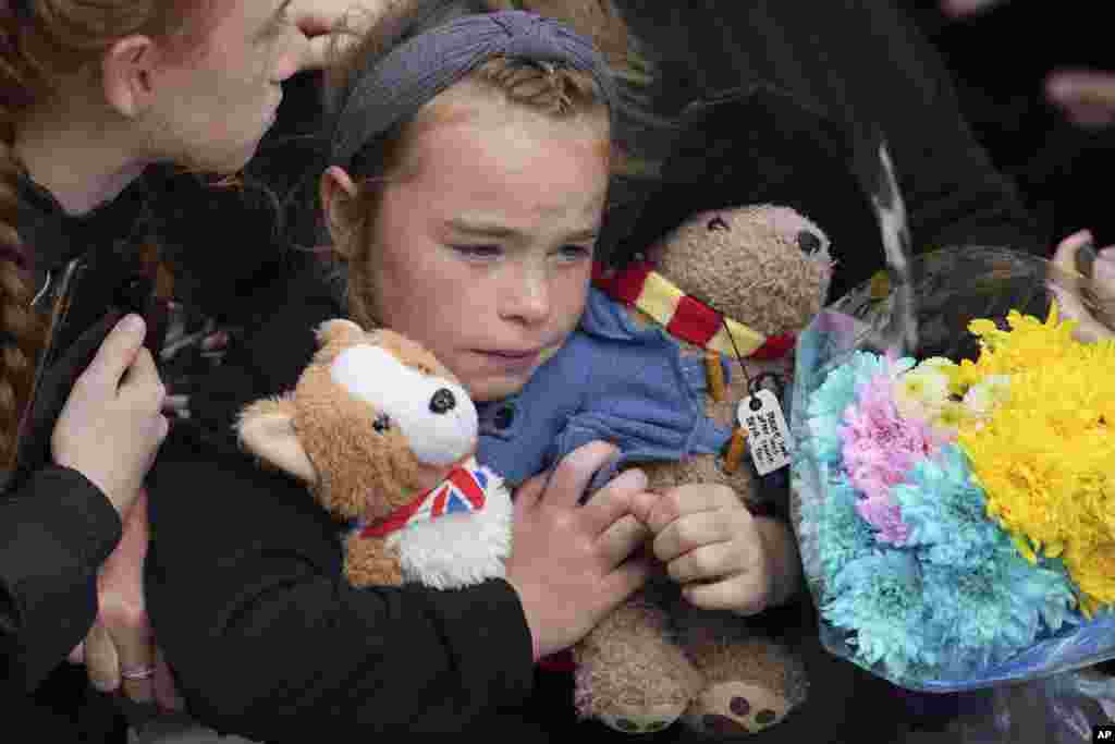A young girl holds a Paddington bear and a Corgi dog stuffed toys while waiting to watch the Procession of Queen Elizabeth's coffin from the Palace of Holyroodhouse to St Giles Cathedral on the Royal Mile in Edinburgh, Scotland, Sept. 12, 2022. 
