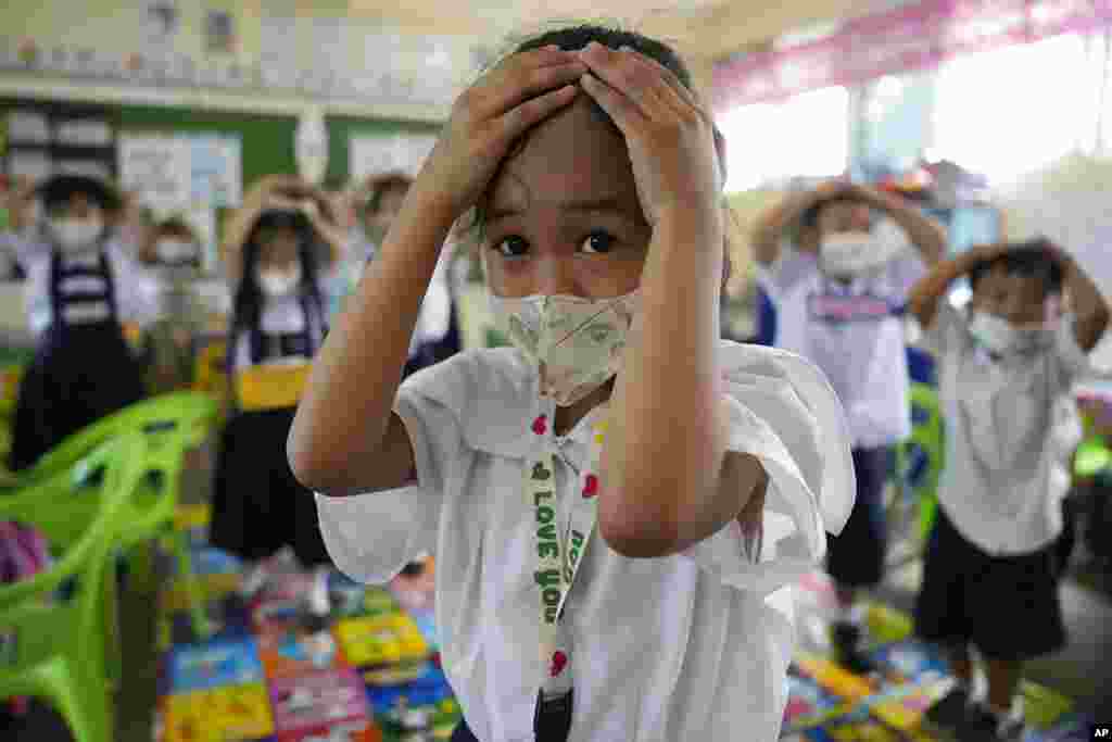 A student places her hands on her head for protection during an earthquake preparation activity at an elementary school in Metro Manila, Philippines.