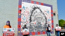 FILE - Activists hold signs promoting Native American participation in the US census in front of a mural of Crow Tribe historian and Presidential Medal of Freedom recipient Joe Medicine Crow on the Crow Indian Reservation in Lodge Grass, Mont., Aug. 26, 2020.