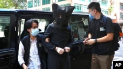 FILE: A hooded suspect is accompanied by police officers to search for evidence at office in Hong Kong, July 22, 2021.