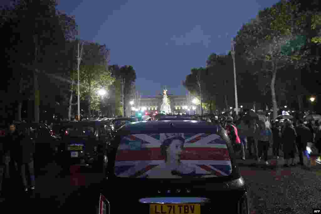 بکنگھم پیلس کے قریب سے ایک ٹیکسی گزر رہی ہے جس پر ملکہ الزبتھ دوم کی تصویر چسپاں ہے۔ 8 ستمبر 2022۔
