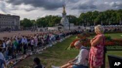 People stand in line after laying flowers for Queen Elizabeth II in front of Buckingham Palace, in London, Sunday, Sept. 11, 2022.