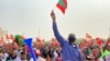 FILE: A man raises a small party flag in the crowd. Cazenga, Luanda. Taken 8.22.2022