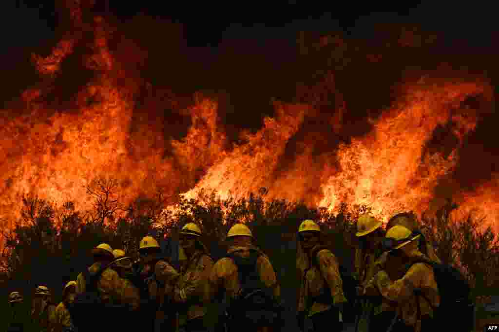 CalFire firefighters turn away from the fire to watch for any stray embers during a firing operation to build a line to contain the Fairview Fire near Hemet, California, on Sept. 8, 2022.