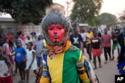 Los miembros de la sociedad secreta de baile Gule Wamkulu con máscaras sangrientas y trajes coloridos caminan por las calles de camino a su actuación de danza ritual en Harare, Zimbabue, el 23 de octubre de 2022.