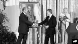 FILE - President Jimmy Carter shakes hands with former President Gerald R. Ford in the White House in Washington on May 24, 1978, during a ceremony at which a portrait of Ford was unveiled.
