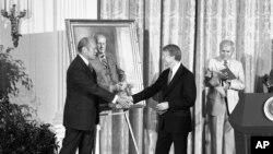 ARHIVA - Predsednik Džimi Karter rukuje se sa bivšim predsednikom Džeraldom Fordom u Beloj kući 24. maja 1978. za vreme otkrivanja Fordovog portreta.