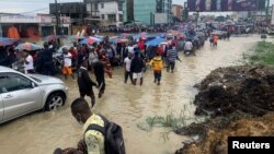 People make their way through a flooded street after heavy rains in Douala, Cameroon, August 12, 2021. The city digs more and more wells trying to find fresh water for its growing population. 