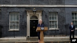 New British Prime Minister Liz Truss speaks outside Downing Street as her husband, Hugh O'Leary, listens, in London, Sept. 6, 2022 after returning from Balmoral in Scotland where she was formally appointed by Britain's Queen Elizabeth II. 