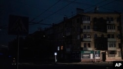 A man crosses a pitch-black street in Kharkiv, Ukraine, Sunday, Sept. 11, 2022. The city appeared to be under a complete blackout with no light visible in the city where a fire raged in a power station reportedly hit in a strike. (AP Photo/Leo Correa)