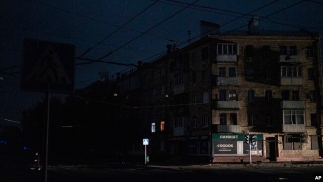 A man crosses a pitch-black street in Kharkiv, Ukraine, Sunday, Sept. 11, 2022. The city appeared to be under a complete blackout with no light visible in the city where a fire raged in a power station reportedly hit in a strike. (AP Photo/Leo Correa)