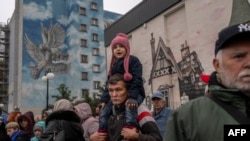 A man holds a child as people wait for blankets and flashlights during an aid supply distribution in the center of Kherson on Nov. 17, 2022.