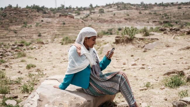 FILE - A woman attempts to get a mobile phone signal after most of an area was in blackout, in Samre, southwest of Mekele in Tigray region, Ethiopia, on June 20, 2021.