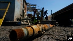 FILE - An oil well worker moves equipment at a site on a ranch where an orphaned well was plugged, May 18, 2021, near Refugio, Texas.