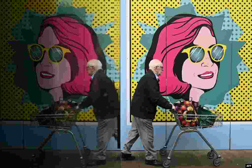 A man pushes a cart past colorful boards put up at a closed shop in Chester, Britain.