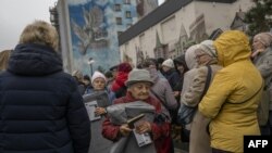 Local residents hold blankets and lamps during an aid supply distribution in the center of Kherson, Ukraine, on Nov. 17, 2022. 